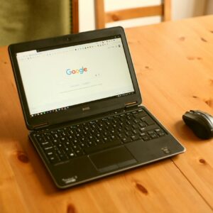 Black laptop and mouse on a wooden desk with Google homepage open.