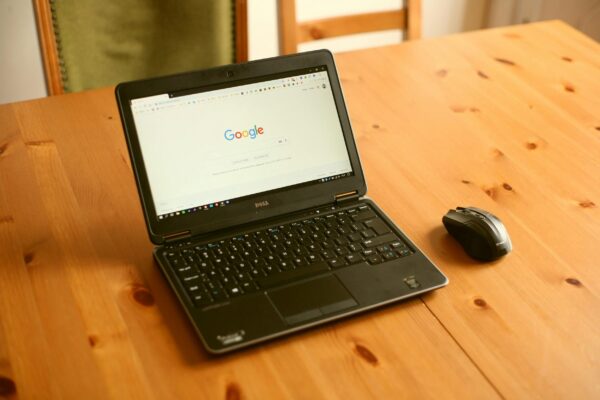 Black laptop and mouse on a wooden desk with Google homepage open.